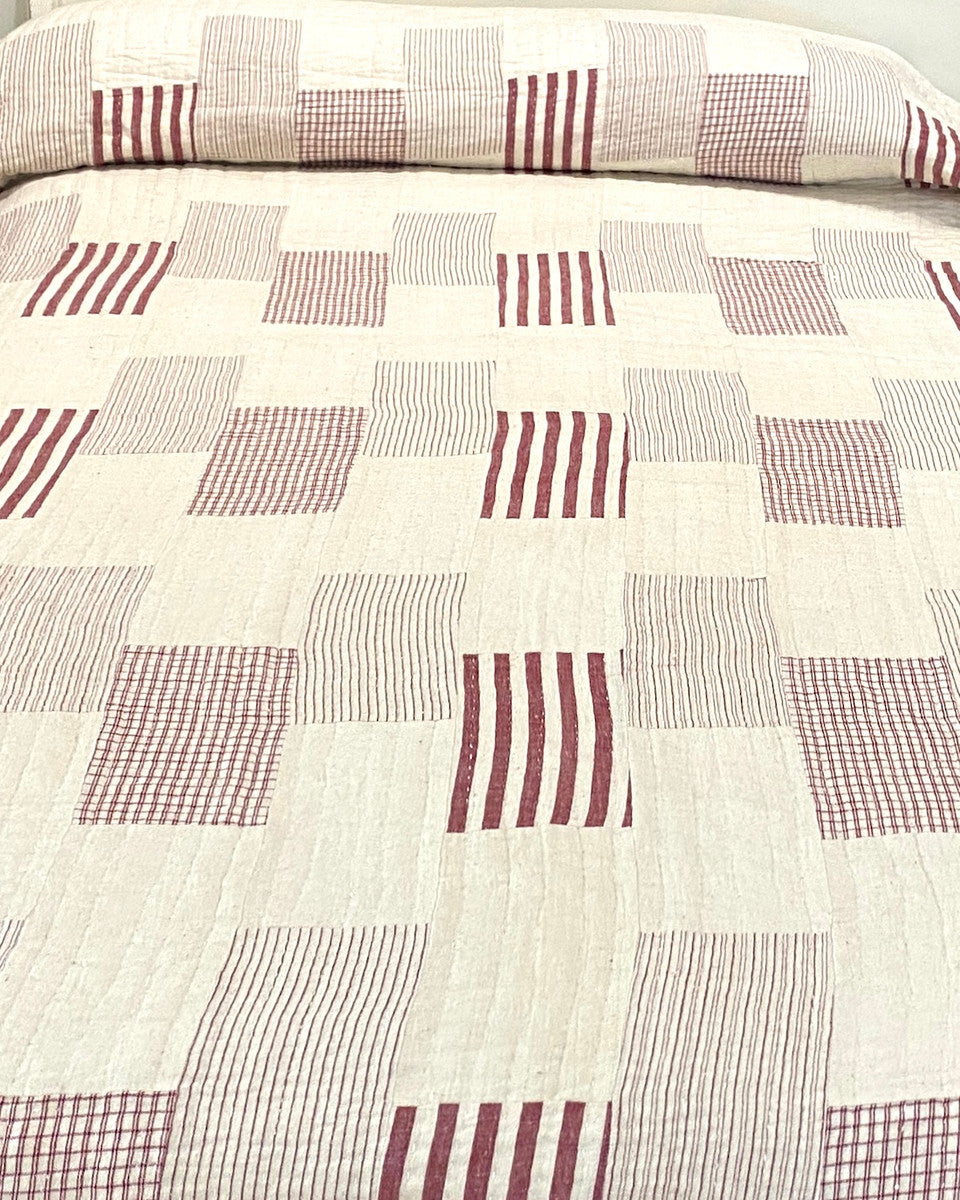 Handwoven Organic Cotton Patchwork Hand Stitched Queen Quilt India. his patchwork quilt has 4 different striped patterns in chalky red and natural white, and solid natural white blocks There are rows of white hand stitching one inch apart. The back is solid off-white natural cotton. It is two layers with a lightweight cotton batting inside.