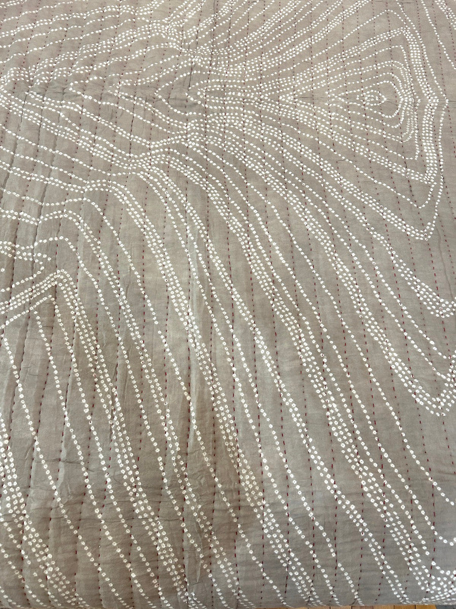 pattern view One-of-a-kind bandhani dyed and hand stitched cotton quilt by Jabbar and Abdullah Khatri, internationally acclaimed folk artists, Gujarat, India. This quilt is a work of art! The design is a organic flowing design of fine tie dyed pattern and the whole quilt has rows of red hand stitching. The rows 1 inch apart. Colors: taupe tan with white dots. The quilt has a thin cotton batting. This is a hand dyed fabric, irregularities are to be expected. The backing in handwoven cotton cloth.