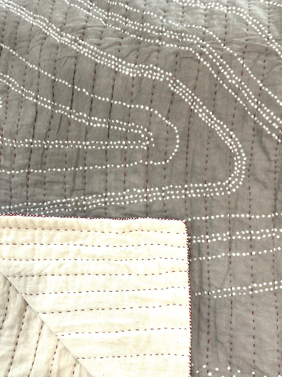 detail both sides One-of-a-kind bandhani dyed and hand stitched cotton quilt by Jabbar and Abdullah Khatri, internationally acclaimed folk artists, Gujarat, India. This quilt is a work of art! The design is a organic flowing design of fine tie dyed pattern and the whole quilt has rows of red hand stitching. The rows 1 inch apart. Colors: taupe tan with white dots. The quilt has a thin cotton batting. This is a hand dyed fabric, irregularities are to be expected. The backing in handwoven cotton cloth.