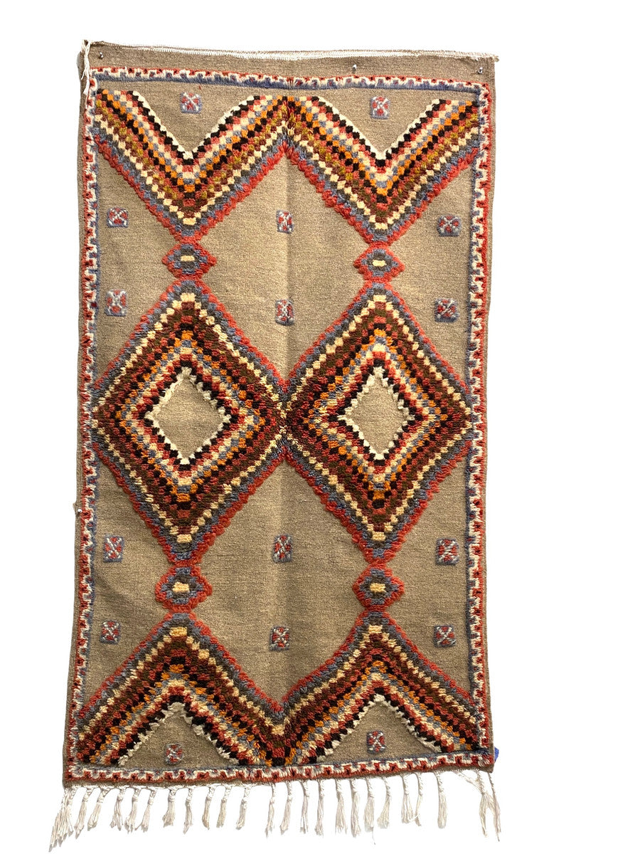 Handwoven and hand knotted Ahknif wool rug. Hand spun wool with a natural grey tightly woven ground and a short pile design of diamonds, squares and a patterned border. . Colors of the short knotted pile: chalky red, washed sky blue, dark grey, off-white, washed chalky red brown, red brown, chalky saffron and cream. There is a braided fringe at one end.