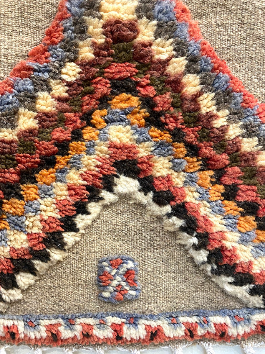 detail 1 Handwoven and hand knotted Ahknif wool rug. Hand spun wool with a natural grey tightly woven ground and a short pile design of diamonds, squares and a patterned border. . Colors of the short knotted pile: chalky red, washed sky blue, dark grey, off-white, washed chalky red brown, red brown, chalky saffron and cream. There is a braided fringe at one end.