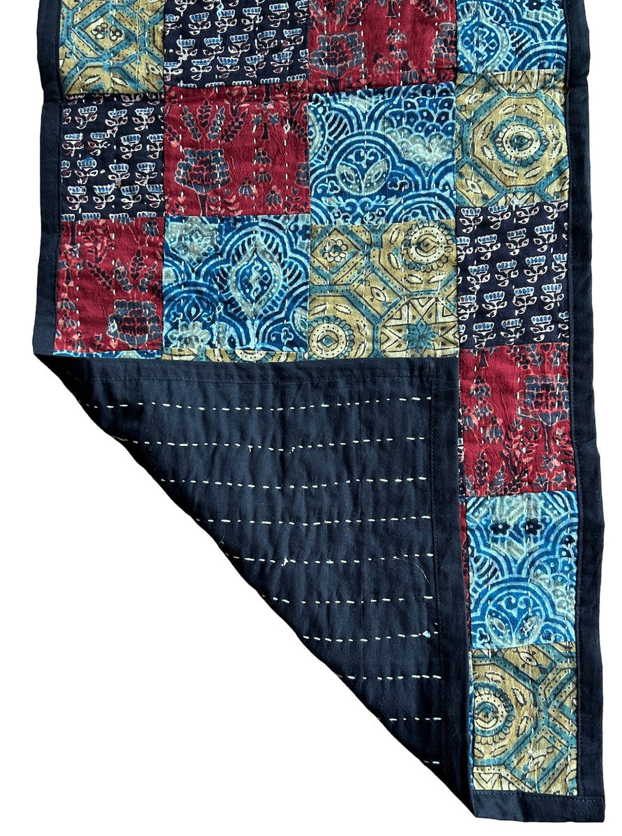 detail both sides Handmade table runner of block printed fabrics. The fabrics are made with several wooden blocks using the traditional Ajarakh natural dye technique. The fabric is then sewn into a patchwork of various colors and patterns.  Beautiful combination of colors: indigo blue, brick red, black, greenish gold, pale blue grey and more. 1" solid black edging around. The back is solid black with white stitching. This can be reversible 

