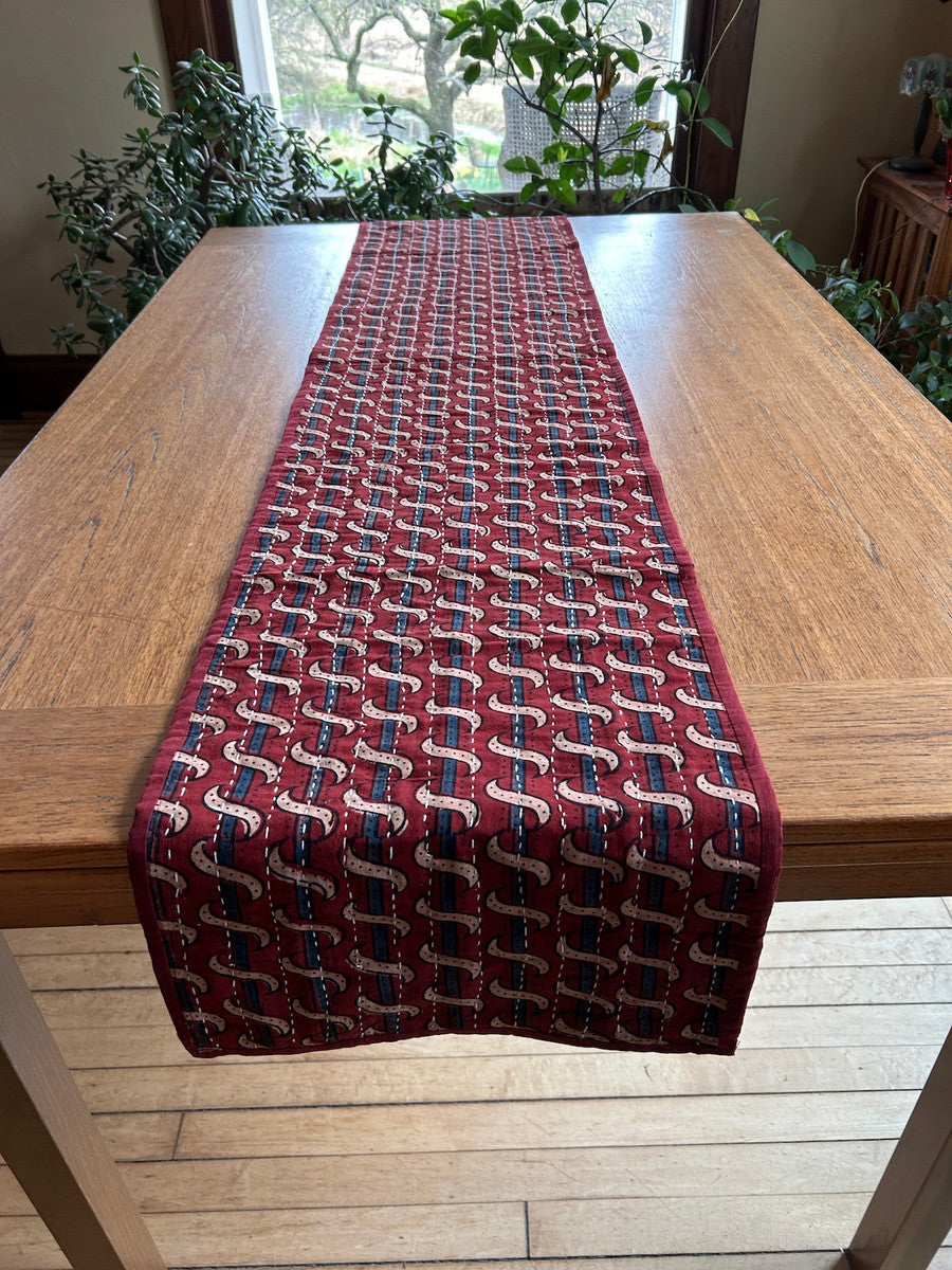 side B Handmade table runner of block printed fabrics. The fabrics are made with several wooden blocks using the traditional Ajarakh natural dye technique. The fabric is then sewn into a patchwork of various colors and patterns.  Beautiful combination of colors: indigo blue, brick red, black, greenish gold, pale blue grey and more. 1" solid brick red edging around. The back is solid brick red with white stitching. This can be reversible 