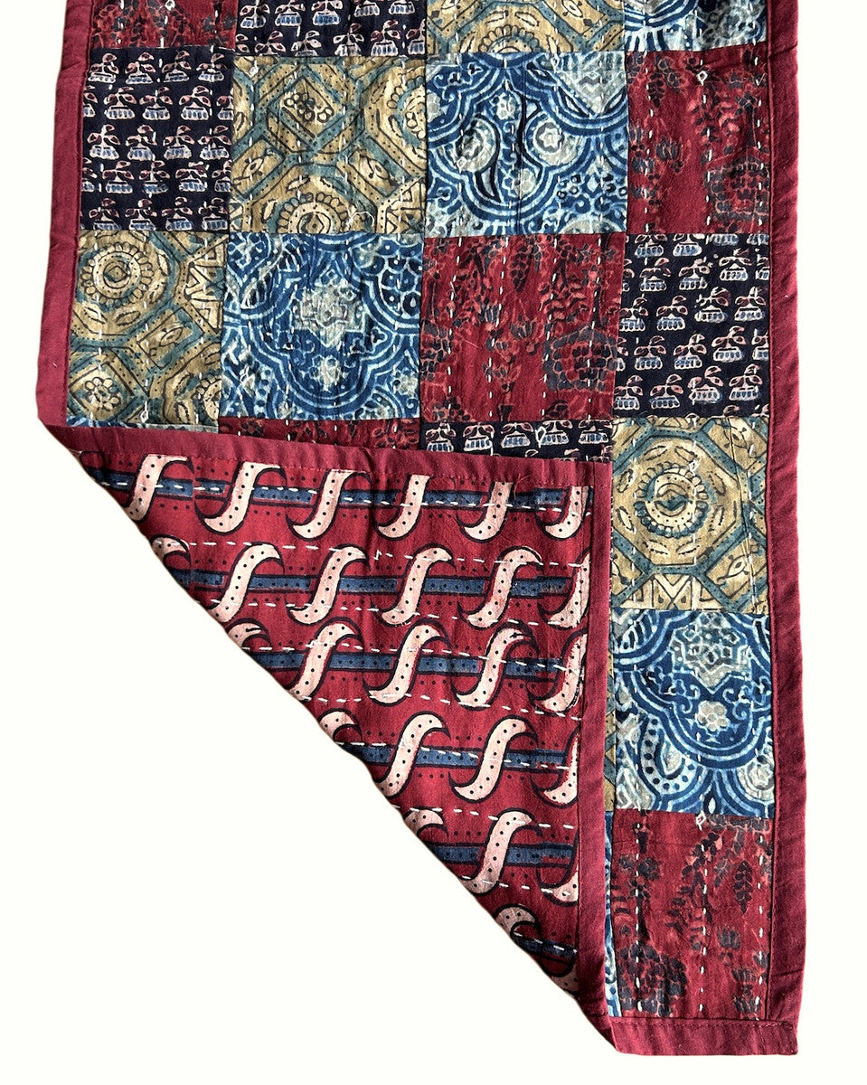 detail both sides Handmade table runner of block printed fabrics. The fabrics are made with several wooden blocks using the traditional Ajarakh natural dye technique. The fabric is then sewn into a patchwork of various colors and patterns.  Beautiful combination of colors: indigo blue, brick red, black, greenish gold, pale blue grey and more. 1" solid brick red edging around. The back is solid brick red with white stitching. This can be reversible 