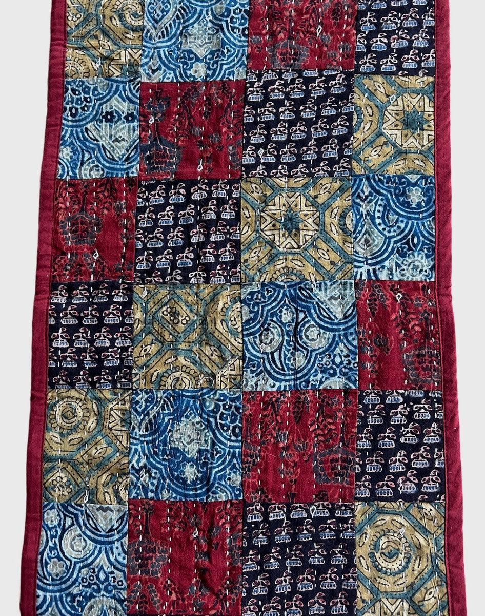 detail Handmade table runner of block printed fabrics. The fabrics are made with several wooden blocks using the traditional Ajarakh natural dye technique. The fabric is then sewn into a patchwork of various colors and patterns.  Beautiful combination of colors: indigo blue, brick red, black, greenish gold, pale blue grey and more. 1" solid brick red edging around. The back is solid brick red with white stitching. This can be reversible 