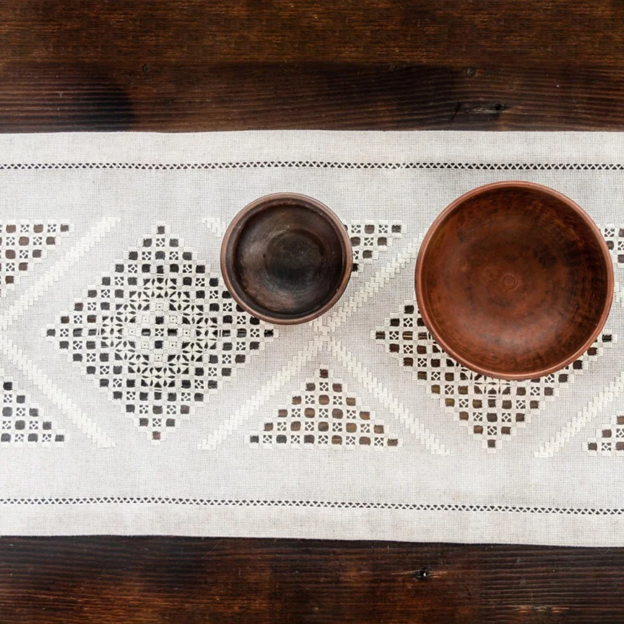 Linen embroidered table runner from ukraine. wo wooden bowls on a decorative white tablecloth with geometric patterns on a wooden surface.