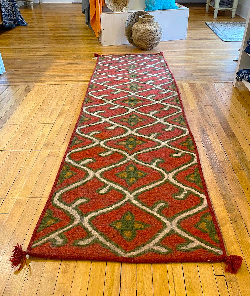 The floral lattice pattern colors are natural white, deep olive and tobacco on a red field There is a dark red colored woven border sewn around the whole rug