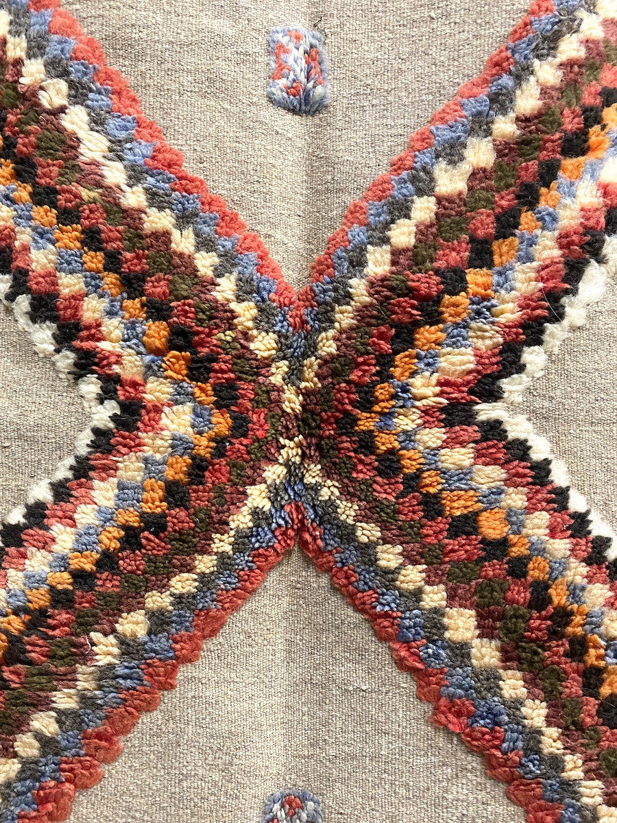 detail 2 Handwoven and hand knotted Ahknif wool rug. Hand spun wool with a natural grey tightly woven ground and a short pile design of diamonds, squares and a patterned border. . Colors of the short knotted pile: chalky red, washed sky blue, dark grey, off-white, washed chalky red brown, red brown, chalky saffron and cream. There is a braided fringe at one end.